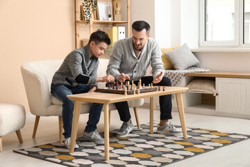 Wall Mural - Father and his little son playing chess on sofa at home