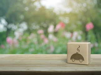 Wall Mural - Restaurant cloche icon on wood block cube on wooden table over blur pink flower and tree in park, Business food delivery online concept