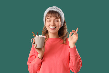 Canvas Print - Pretty young woman holding cup of hot chocolate with marshmallows and cinnamon on green background