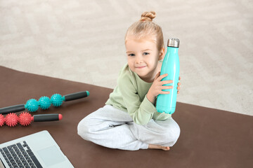 Poster - Cute little girl sitting on yoga mat with body rollers, laptop and bottle of water in living room