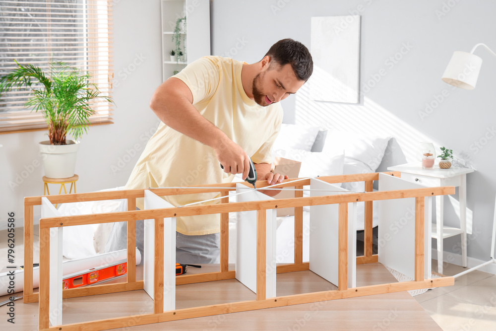 Young man with screwdriver assembling shelving unit in bedroom