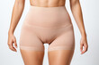 A woman wearing a tight beige waist cincher to shape and compress the tummy, making it apprearing smaller. Female with skin color figure shaping undergarment worn as body shaper and thigh slimmer.