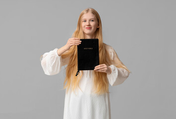 Wall Mural - Beautiful young happy woman with Bible on grey background