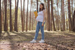 Full length of pregnant woman wearing casual clothing holding yoga mat while standing in spring forest preparing for workout in open air enjoying yoga in wood