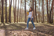 Confident serious pregnant woman wearing casual clothing walking in forest with yoga mat in hands preparing for training outdoor on beautiful nature