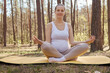 Outside practicing pose during pregnancy. Outdoors sport fertility. Caucasian pregnant woman doing yoga on mat expecting mother meditating in lotus pose