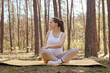 Forest nature pregnant. Concentrated Caucasian brown haired pregnant woman doing yoga on mat looking away stretching her body doing workout in park