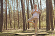 Full length of slim sporty athletic Caucasian pregnant woman doing sports exercising on mat standing in yoga pose and with praying gesture practicing yoga in forest