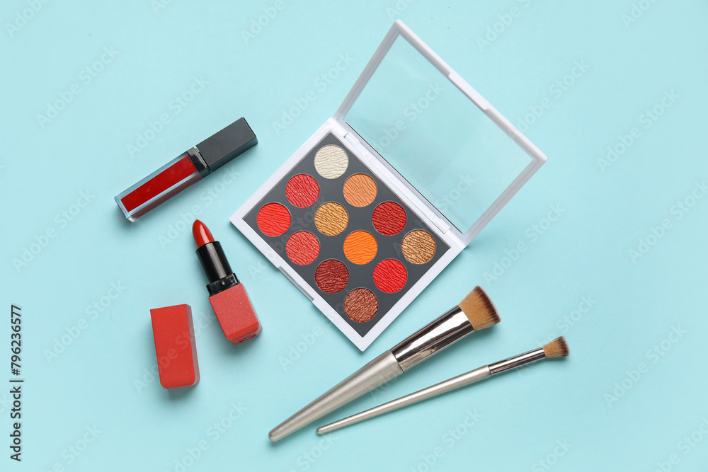 Palette of colorful eyeshadows with brushes and lipsticks on blue background. Top view