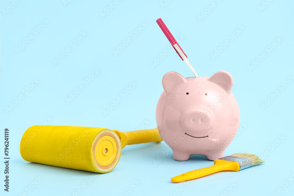 Piggy bank with paint roller and brush on blue background