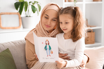 Poster - Little girl with greeting card and her Muslim mother on sofa at home