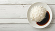 Plate with boiled rice and soy sauce on white wooden