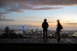 People in silhouette walking on the boardwalk. Sky Tower and cityscape in the distance. Motion blur by slow shutter speed. Mt Eden summit at dawn. Auckland.
