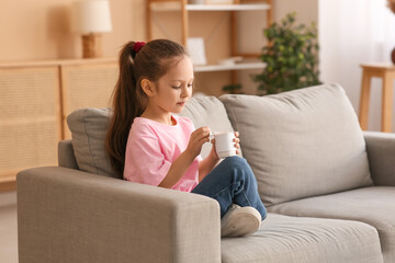 Canvas Print - Cute little girl sitting on sofa and opening yogurt pack at home