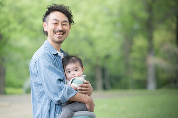 Dad holding a baby in the fresh green outdoors Image of ikumen or male childcare and parenting Looking at the camera