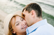 Male kisses female on cheek on beach ocean and enjoys sunny summer day. Man embraces woman on sand sea. Couple in love hugging and kissing on seashore. Spending time together. Closeup face. Top view