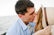 Man embraces woman stands on sand sea. Female kisses male on beach ocean and enjoys sunny summer day. Couple in love hugging and kissing each other on seashore. Spending time together. Closeup face.