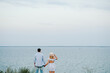 Man and woman hold hands on seashore spending time together. Couple in love look at the sea in the distance on the edge of a cliff. Female and male on beach ocean and enjoying summer day. Back view.