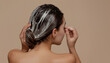 © Oleksiy - Young woman applying hair mask on beige background, back view