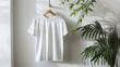 White t-shirt on wooden hanger against white wall with palm leaf shadows.