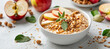 Oatmeal served with peanut butter, fresh apple slices and granola in a white bowl