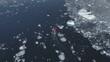 Motor boat floats among the Antarctic ice floes and icebergs. Aerial tracking drone flight overview of south pole ocean landscape. Rubber boat sailing in open water brash ice.