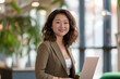 © 수동 김 - A photo of an attractive asian woman standing in the middle, smiling and holding her laptop computer while dressed for work in business casual attire with shoulder length curly hair
