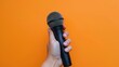 Hand securely holding a microphone, captured in portrait orientation with a vivid orange background, emphasizing dynamic sales and marketing strategies