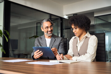 Happy busy male mentor executive manager training young female employee at work. Two diverse professional business team people working on financial management in office using digital tablet.