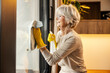 A tidy senior woman is cleaning windows at home.