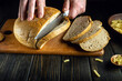 Slicing rye bread on a kitchen board with a knife in the hands of a cook before breakfast.