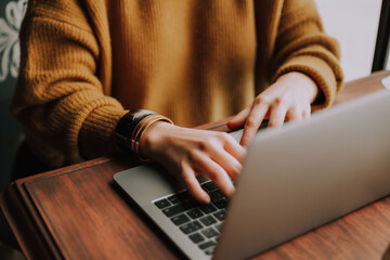 Cropped image of female hands typing on a laptop keyboard while sitting in a cafe
