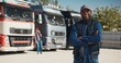 Happy African American trucker standing before camera and smiling with joy. Having positive feelings after work while driving his lorry. Working at logistics job. Export or import concept.