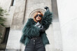 Fashion beautiful stylish woman model with trendy sunglasses in a shaggy jacket with a handbag posing on the street