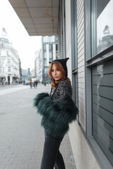 Wall Mural - Stylish lovely beautiful trendy girl in fashion clothes with a hat, shaggy jacket walks in the city. Pretty urban lady