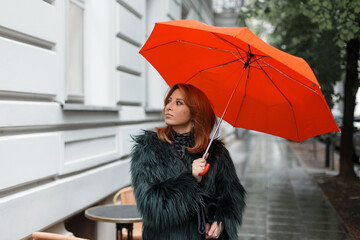 Wall Mural - Fashion beautiful girl in stylish clothes with a bright orange umbrella walks in the city on a rainy day