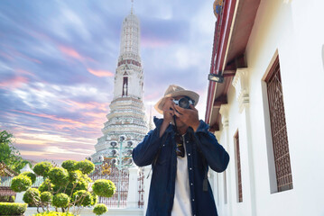 Young Asian traveling backpacker taking photos with camera in Wat Arun in Bangkok, Thailand