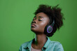 Young African American woman wearing headphones on a green background listening to her favorite music.