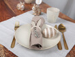 Gedeckter Tisch zu Ostern in gold, weiß, naturfarben mit Besteck, Teller, Serviettenring und Teller