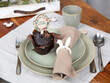 Gedeckter Tisch zu Ostern mit Muffin, Stoffserviette, Besteck, Teller und Kaffeetasse mit Osterhase