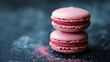 Close-up of pink macarons with tiny crumbs scattered on a dark, textured surface, emphasizing a gourmet treat.
