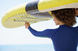 Positive woman in curly hair lifting yellow paddleboard