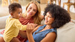 © Monkey Business - Same Sex Female Couple Or Friends Playing With Baby Sitting On Sofa At Home Together
