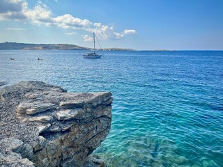 seascape of the island of Malta with a view of a sailboat on the turquoise-colored Mediterranean Sea from a rocky coast under a cloudy sky on a summer day
