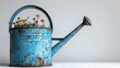 A bright blue watering can sits isolated in a summer garden, ready to quench thirsty flowers