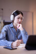 Young asian student women wearing headphone to learning lecture webinar in online class on tablet while thoughtful about educational to writing notes and studying knowledge remote education from home