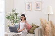 Pregnant woman working on laptop and smart phone in the living room at home