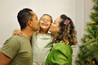 Familia Parda com traços brasileiros com homem, mulher e um menino criança, em uma sala com uma decoração de natal na cor verde.