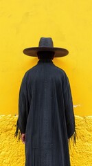 Canvas Print - A man in a black hat and long coat standing against yellow wall, AI