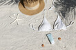 Broad brim straw hat, white bathing suit bra and sunblock tubes. Top view, flat lay, copy space, background.